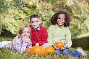 Three young friends sitting on grass with pumpkins smiling