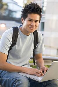 Man sitting on bench outdoors using laptop (selective focus)