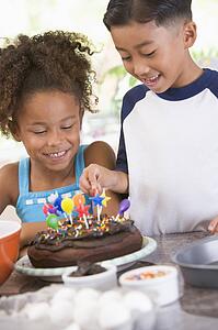 Two children in kitchen with birthday cake smiling