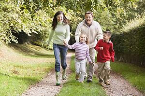 Family outdoors walking on path holding hands and smiling (selective focus)