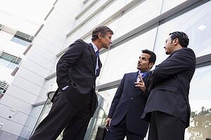 Three businessmen standing outdoors by building talking (high key/selective focus)