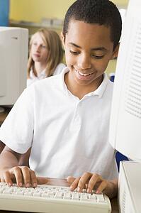 Student at computer terminal typing with student in background (selective focus)
