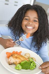 Young girl in kitchen eating chicken and vegetables smiling