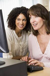 Two women at a computer terminal typing (high key)