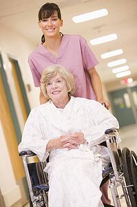 A Nurse Pushing A Senior Woman In A Wheelchair Down A Hospital Corridor