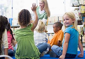 Student in class looking at camera with teacher reading in background (selective focus)