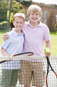 Two young male friends with rackets on tennis court smiling