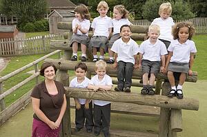 Students sitting outdoors on wooden structure with teacher standing beside them