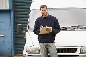 Deliveryperson standing with van writing in clipboard smiling
