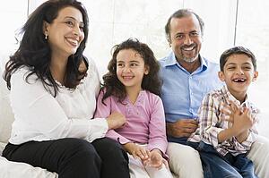 Grandparents sitting in living room with grandchildren smiling (high key)