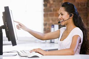 Businesswoman in office wearing headset and pointing at computer monitor