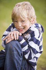 Young boy sitting outdoors dirty and smiling