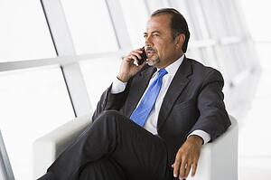 Businessman sitting indoors on cellular phone (high key/selective focus)