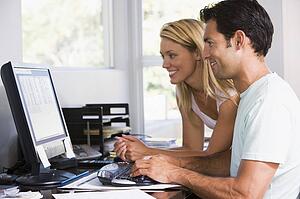 Couple in home office using computer and smiling
