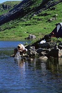 Woman outdoors at campsite washing face in lake