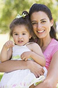 Mother holding daughter outdoors smiling