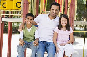 Father and two children sitting on playground structure smiling (selective focus)
