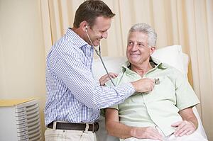 Doctor giving man checkup with stethoscope in exam room smiling