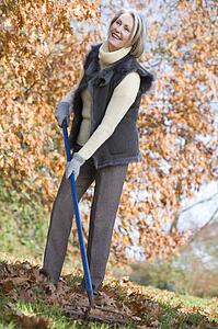 Woman outdoors raking leaves and smiling (selective focus)