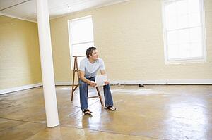 Man sitting on ladder in empty space holding paper smiling