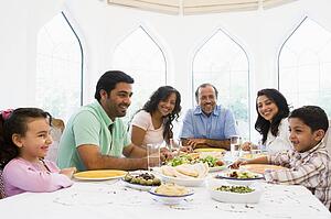 Family sitting at dinner table smiling (high key)