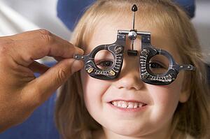 Optometrist in exam room with young girl in chair smiling