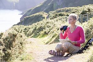 Woman on cliffside path using binoculars