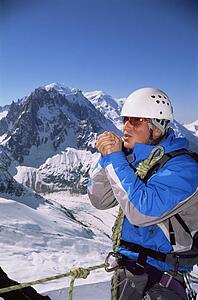 Mountain climber standing in snow on mountain warming up hands (selective focus)
