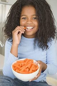 Young girl in kitchen eating carrot sticks smiling
