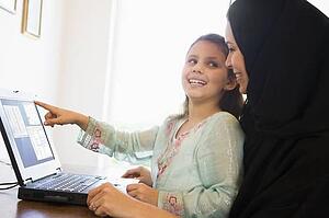 Mother and daughter in office with laptop pointing and smiling (high key/selective focus)