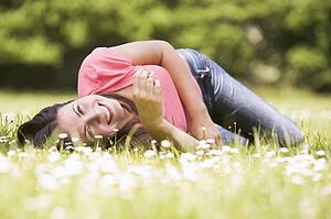 Woman lying outdoors with flower smiling