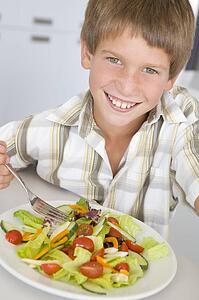 Young boy in kitchen eating salad smiling