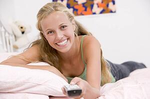 Teenage Girl Lying On Her Bed Changing Television Channels