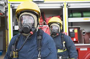 Two firemen in masks standing near fire engine (depth of field)
