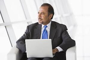 Businessman sitting indoors with laptop looking out window (high key/selective focus)