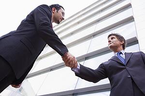 Two businessmen outdoors by building shaking hands (high key/selective focus)
