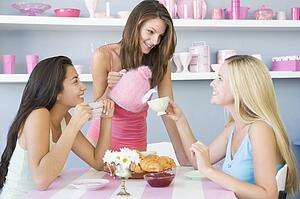 Three young woman sitting at a table having tea and a snack
