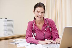Doctor using laptop in doctor's office smiling