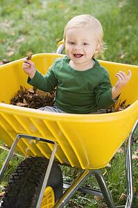 Baby outdoors sitting in wheelbarrow smiling (selective focus)