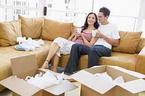 Couple relaxing with coffee by boxes in new home smiling