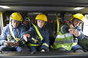 Three firefighters in fire engine wearing helmets with one pointing