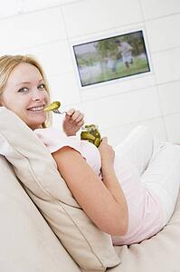 Pregnant woman watching television and eating pickles smiling