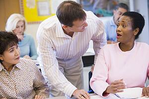 Adult students in class with teacher helping one (selective focus)