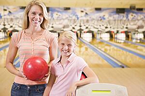 Woman and young girl in bowling alley holding ball and smiling