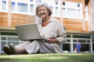 Woman sitting on lawn of school with laptop