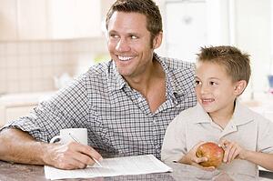 Man and young boy in kitchen with newspaper apple and coffee smiling