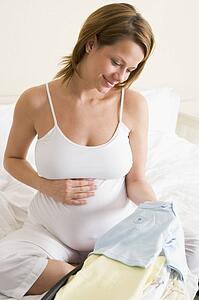 Pregnant woman packing baby clothing in suitcase smiling