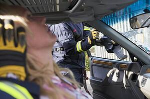 Firefighter cutting out a windshield after an accident with injured woman in foreground (selective focus)