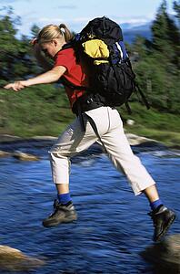 Woman outdoors hiking in scenic location jumping over water (selective focus)