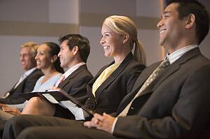 Five businesspeople smiling in presentation room with clipboards